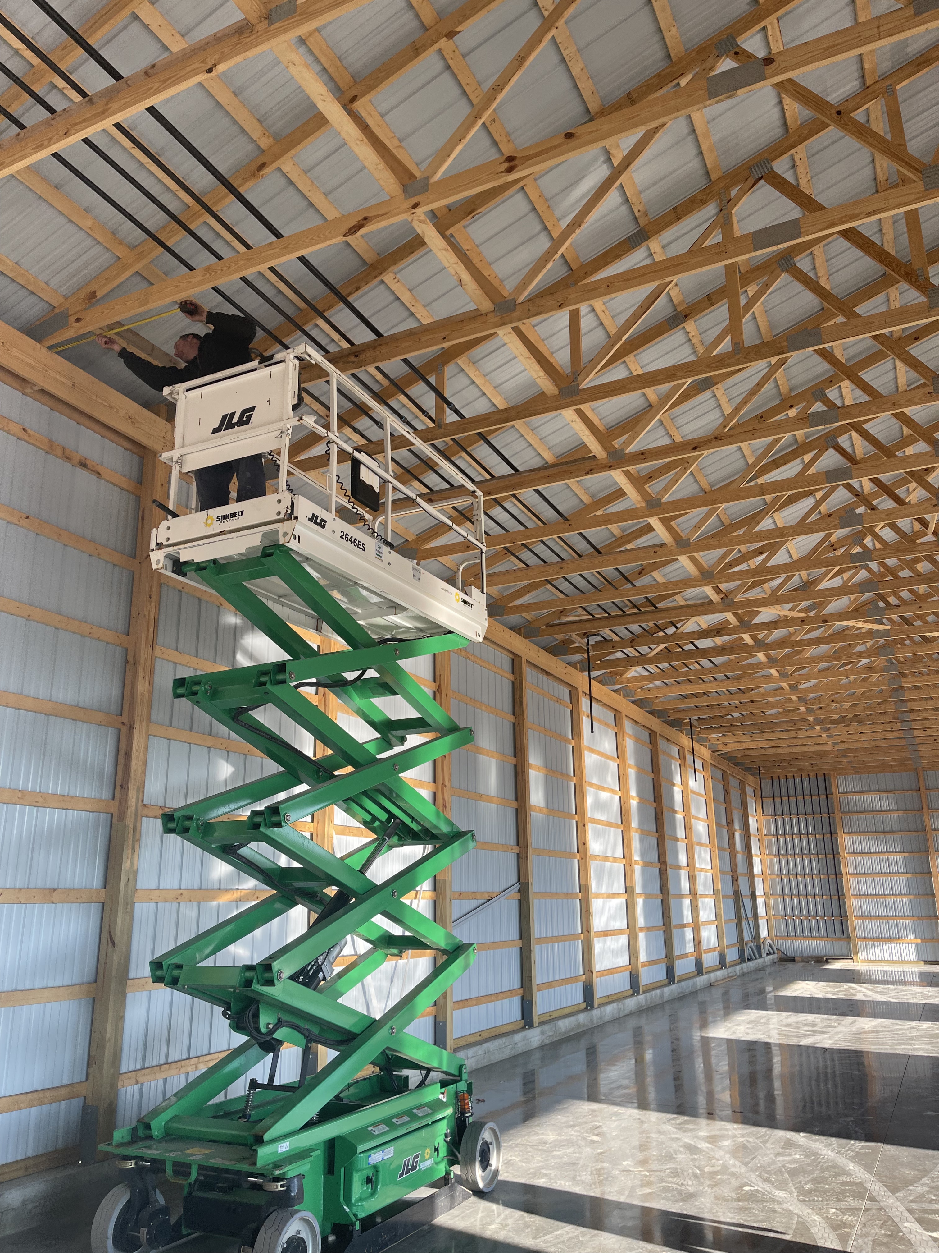 Worker on a green scissor lift installing wiring in a large wooden structure.