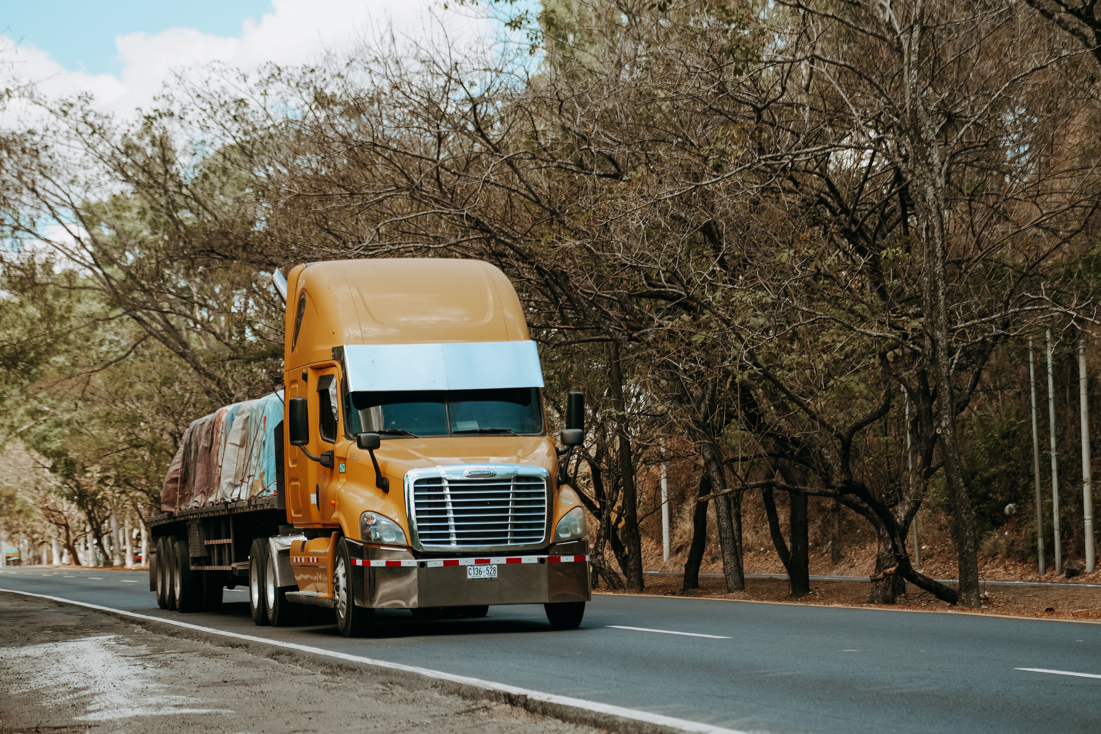 Yellow semi-truck driving on a tree-lined road