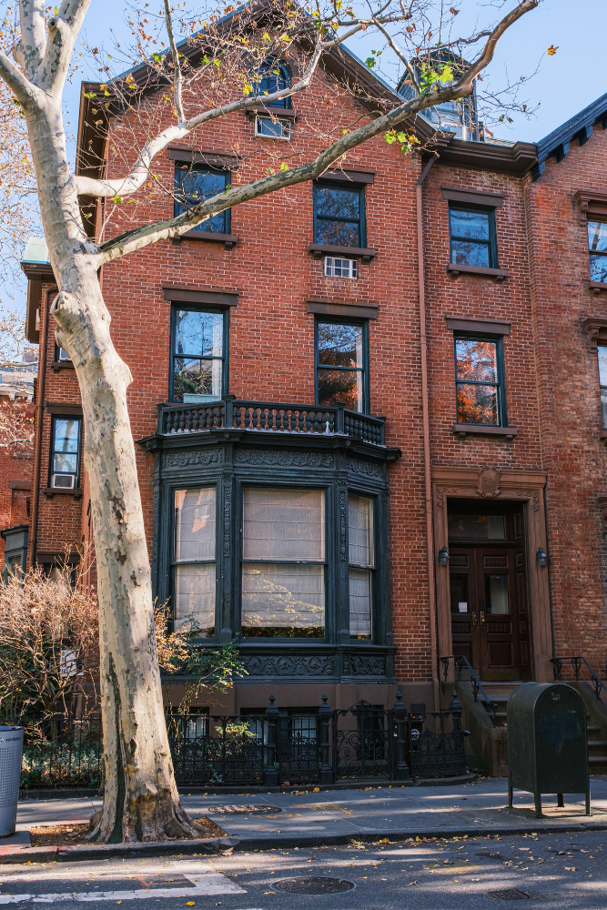 Historic red brick townhouse with bay windows and a tree in the foreground.