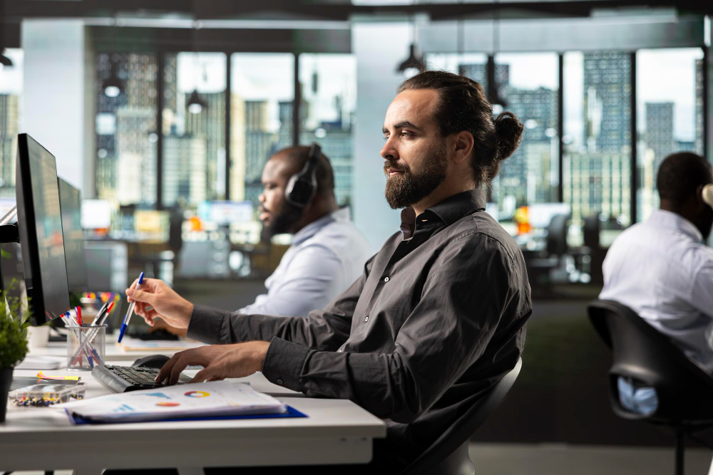 Office workers at desks with computers and headsets in a modern office setting